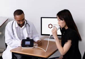 Analyseur de FeNO NIOX VERO® : patiente soufflant dans l’embout du NIOX VERO sous la supervision d’un médecin