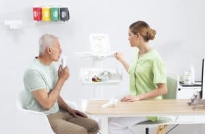 Patient soufflant dans le spiromètre MESI mTABLET SPIRO sous la supervision d’une infirmière