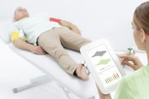 Patient équipé de brassards et capteurs TBI pendant qu’une soignante consulte la tablette MESI