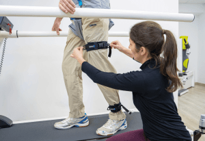 Système d'entraînement à la marche robowalk® : thérapeute ajustant le harnais de soutien sur un patient en rééducation